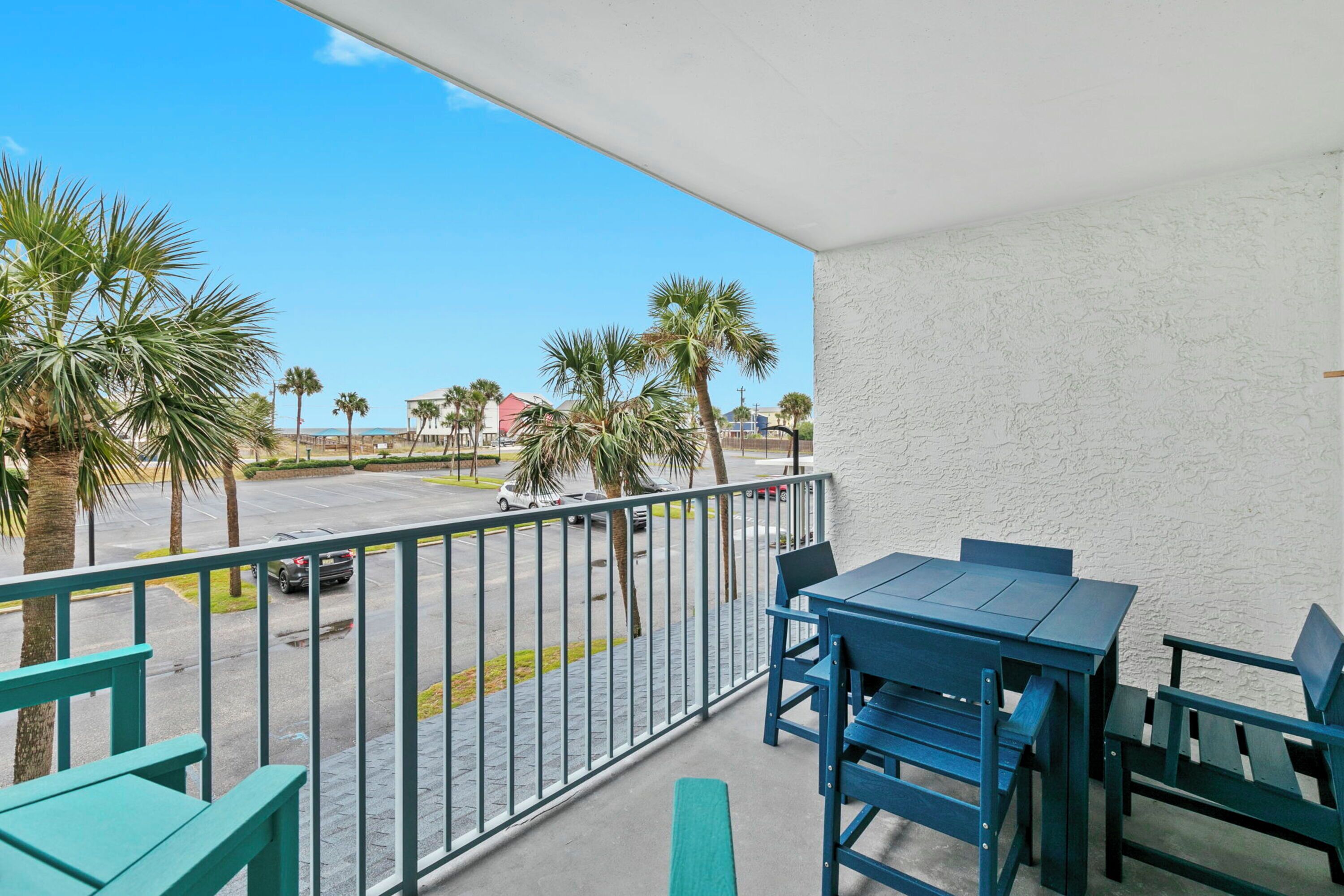 A balcony with a table and chairs, overlooking a street with palm trees and parked cars.