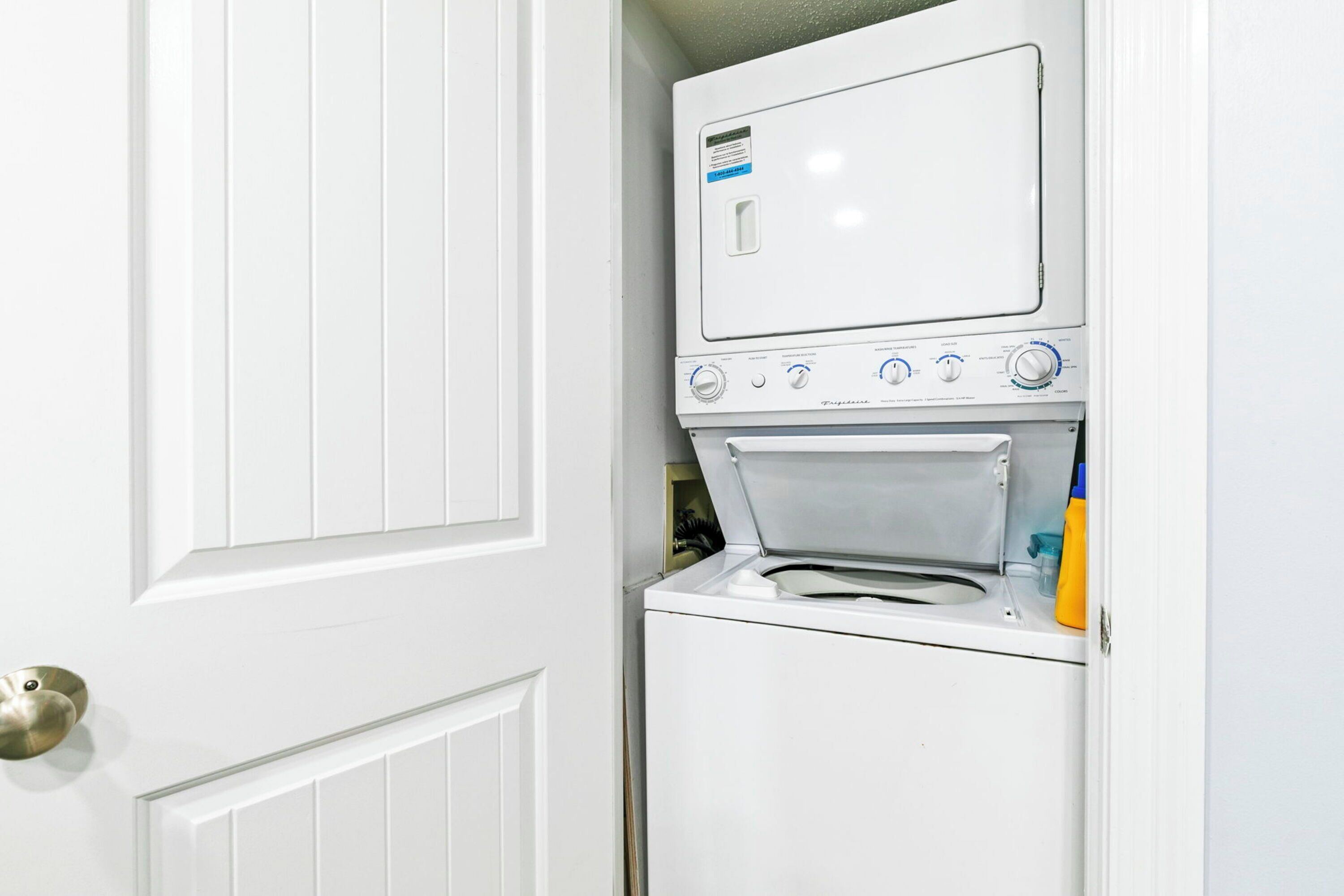 A compact washer and dryer unit installed in a white door, with a small shelf above the dryer for storage.