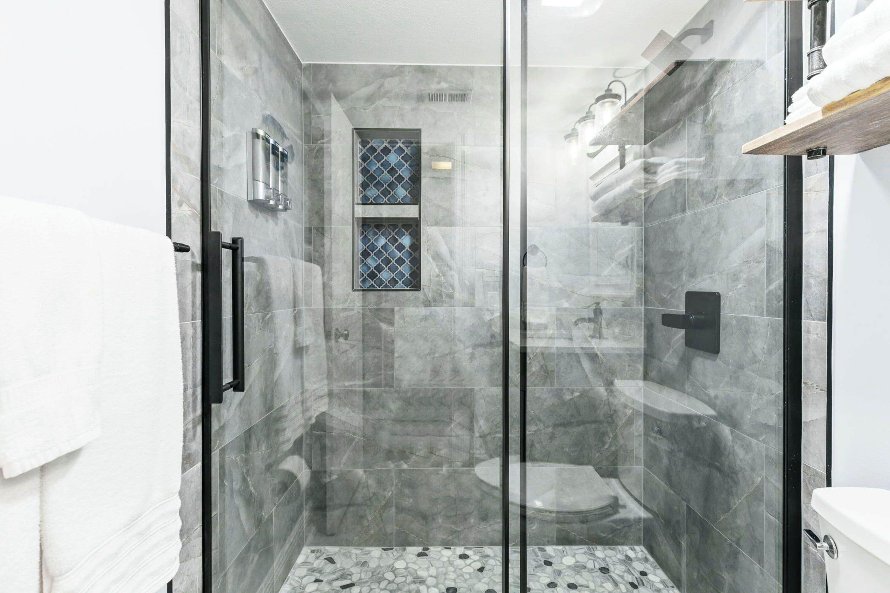 A modern bathroom with a glass-enclosed shower, marble tiles, and a small window.