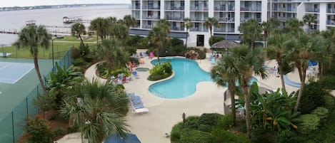 A hotel with a swimming pool, palm trees, and a tennis court.