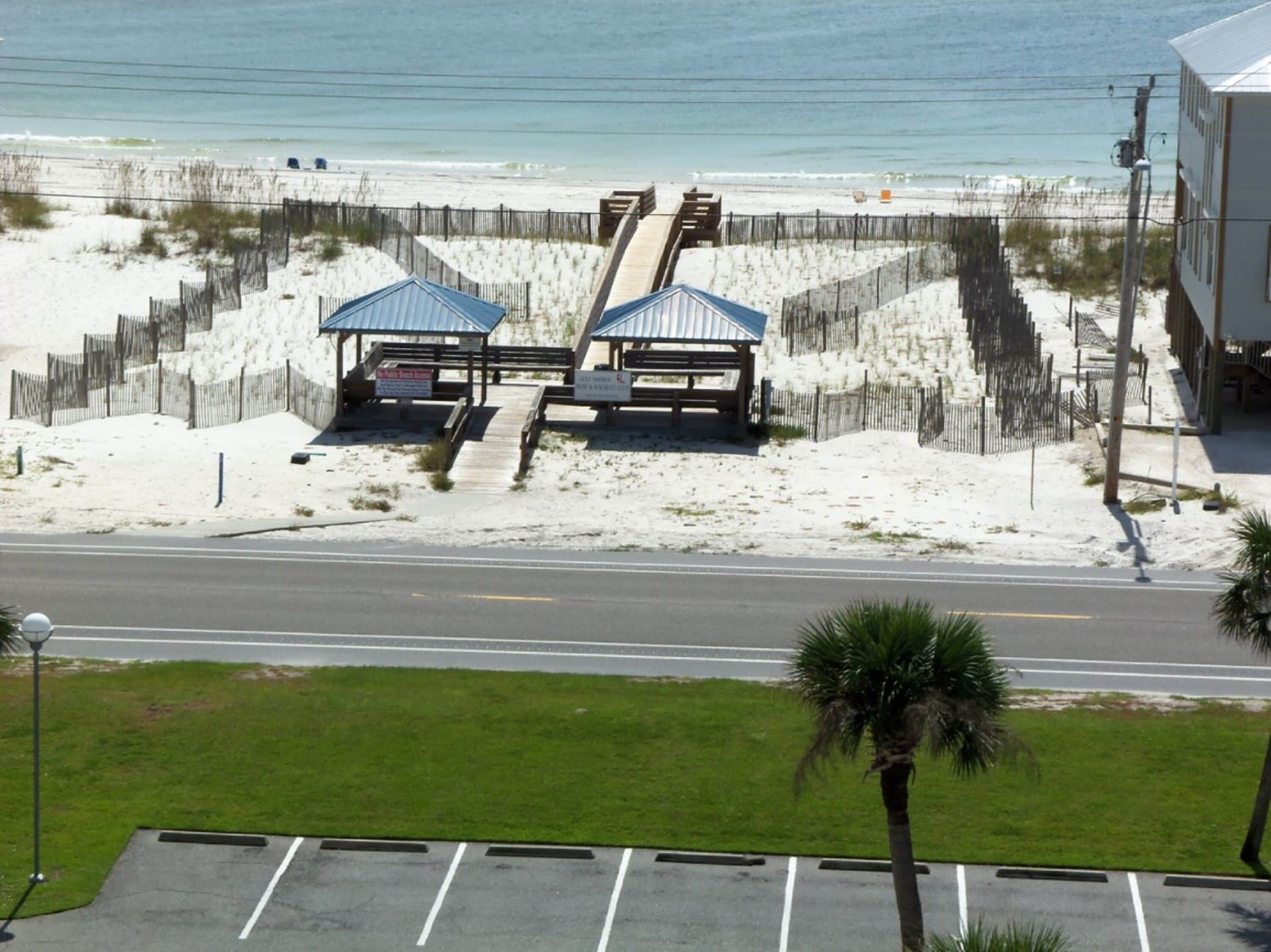 A beachside parking lot with a road leading to beach huts and a fence.