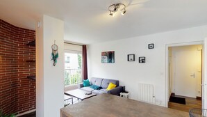 Una sala de estar moderna con una pared de ladrillo decorativa, un sofá gris con cojines coloridos, una mesa de centro de madera y un comedor con una silla de metal.