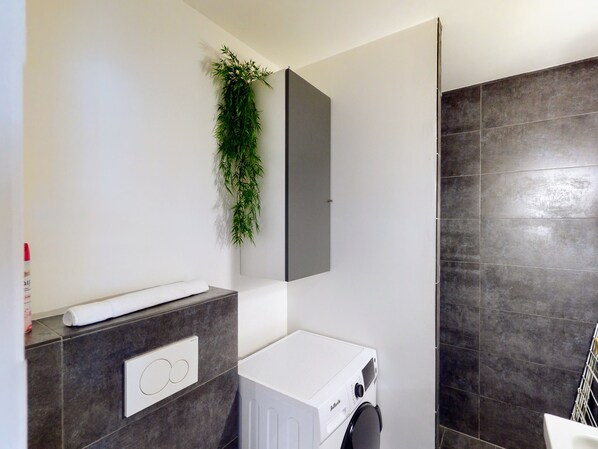 A modern bathroom with a built-in washing machine, a towel dispenser, and a vertical garden.