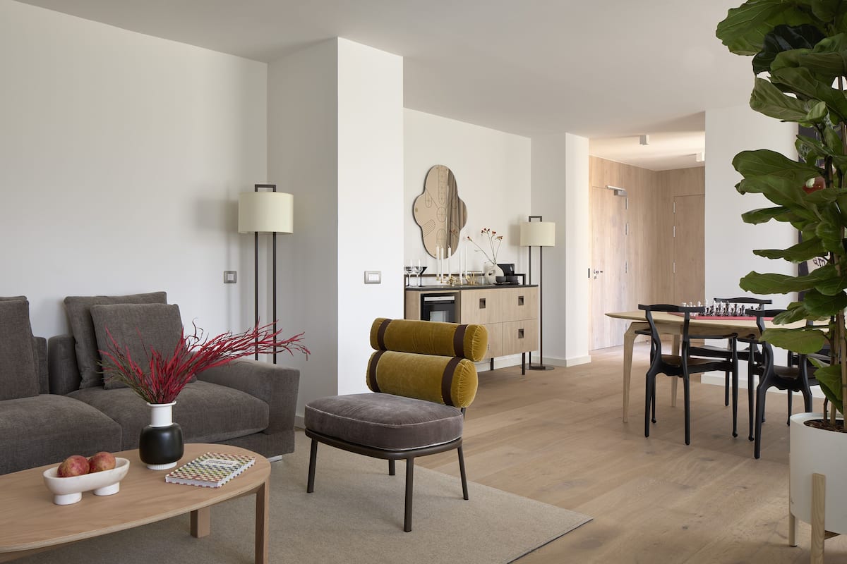 A modern living room with a sofa, ottoman, coffee table, and a dining area with a table and chairs.