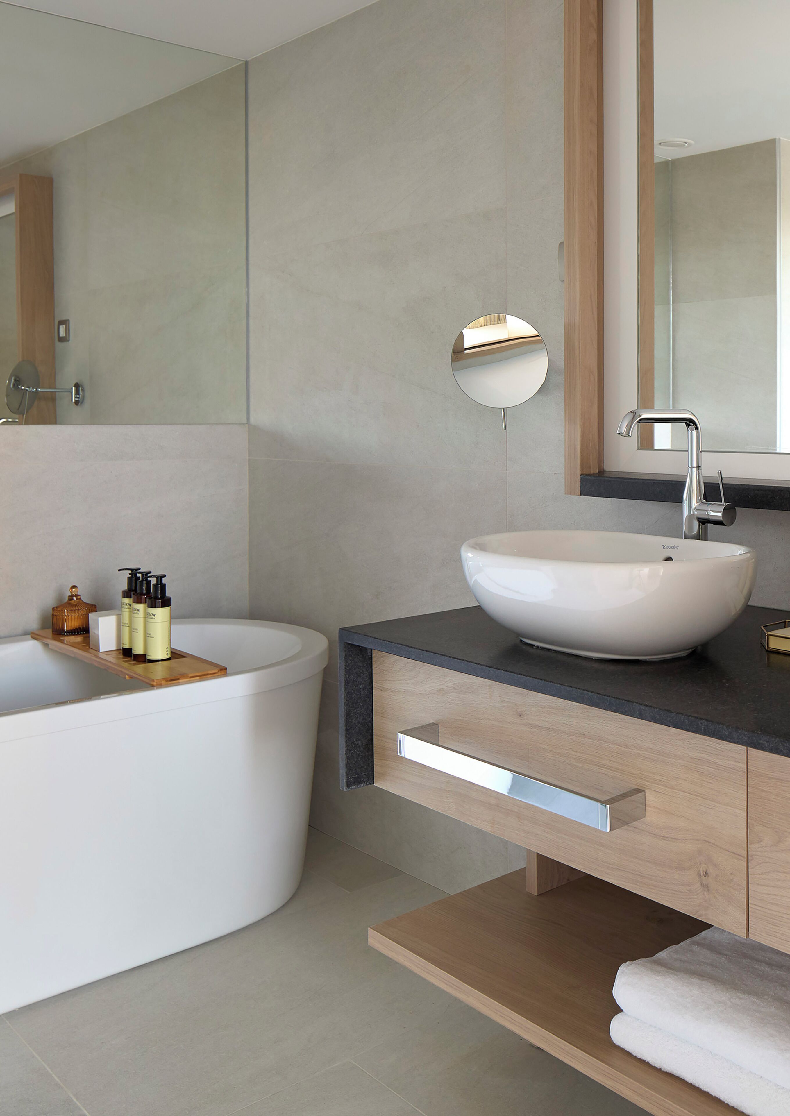 Un baño moderno con una bañera independiente, un lavamanos sobre encimera y un tocador de madera con perchero.