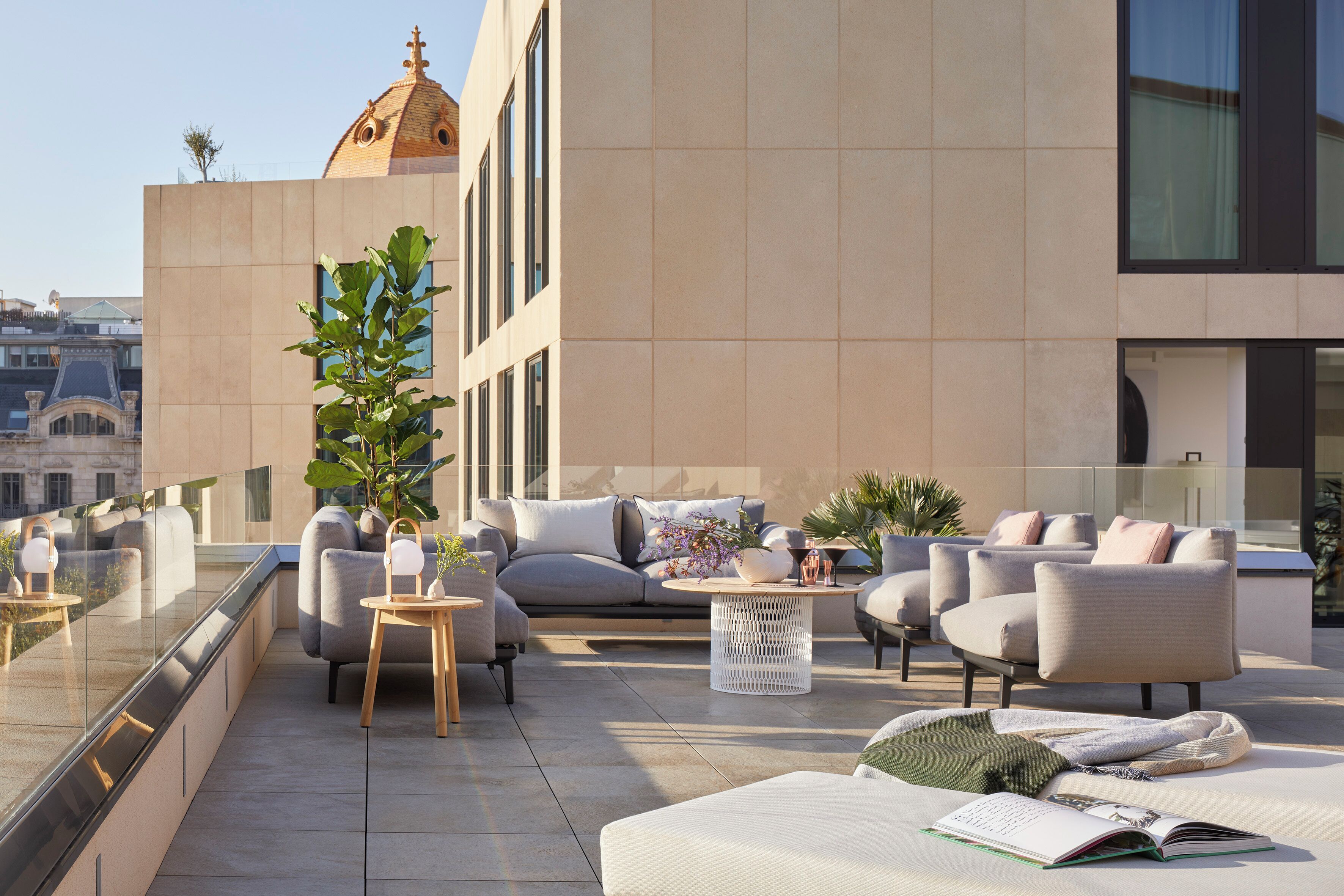 A rooftop terrace with modern outdoor furniture, including sofas and chairs, and a potted plant.