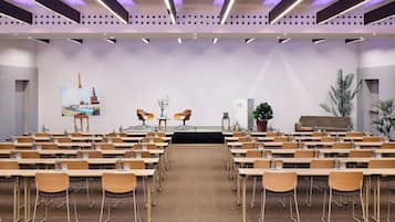 Un salón de conferencias con varias mesas y sillas, un escenario con dos sillas y un cuadro grande en la pared.