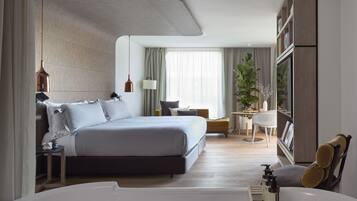 A modern hotel room with a large bed, a sitting area, a small table with a plant, and a large window with curtains.