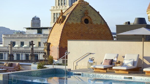 Un espace piscine aménagé sur le toit, avec des chaises longues, une petite table et une vue sur un bâtiment historique en arrière-plan.