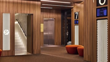 Un vestíbulo moderno con interior de madera, una escalera, un ascensor y asientos naranja.