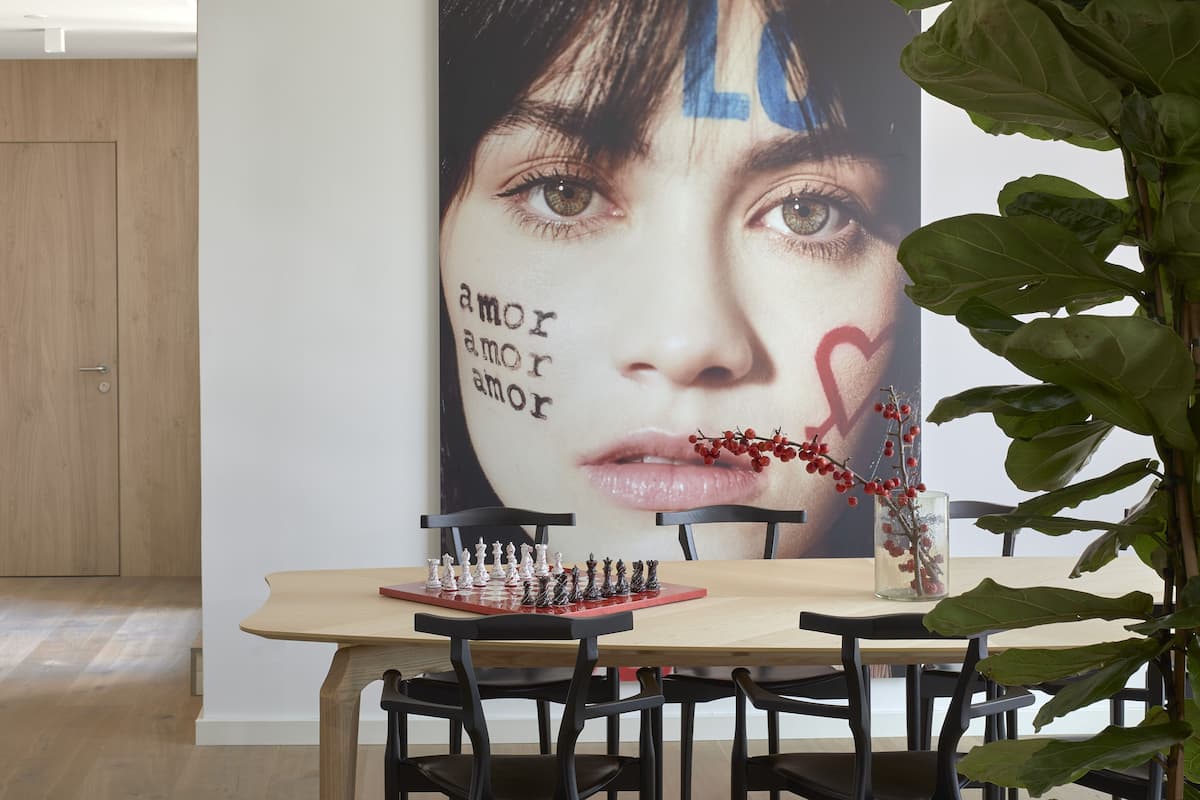 A dining area with a chessboard, chairs, a table, and a large poster on the wall.