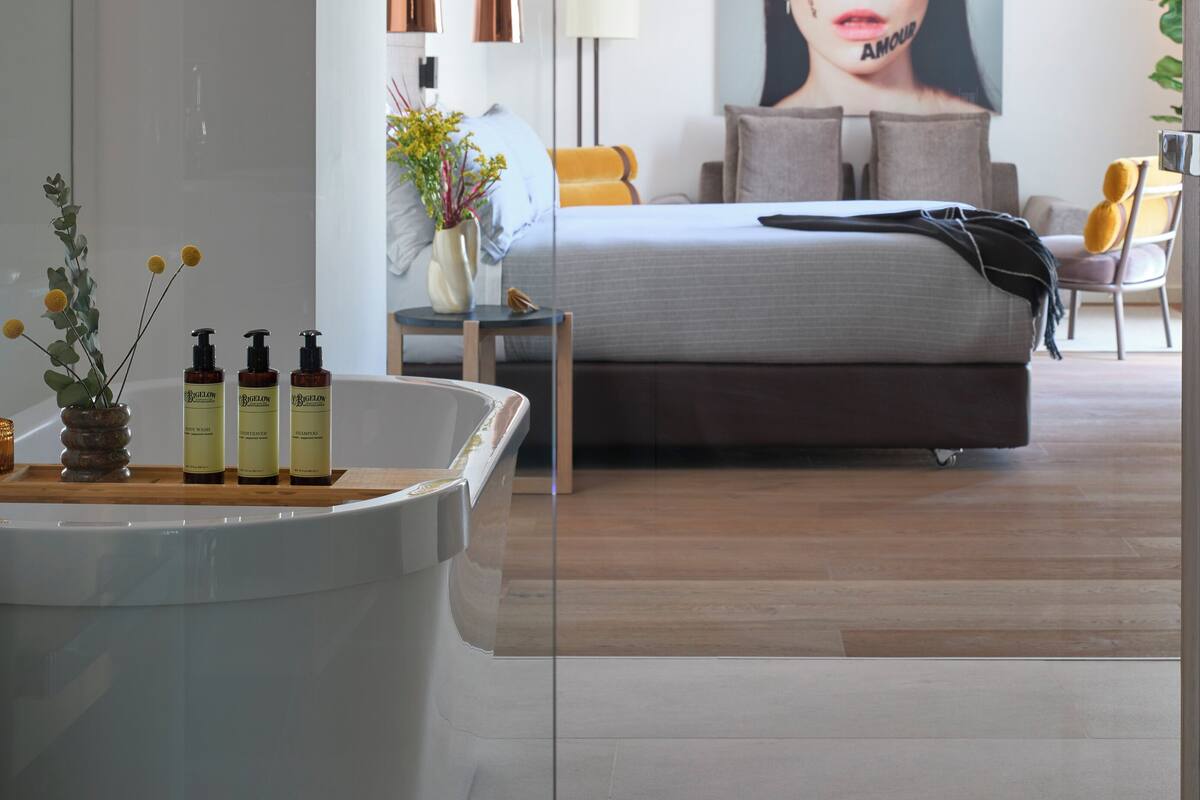 A modern bedroom with a large bed, bedside tables, a lamp, and a wall-mounted artwork.