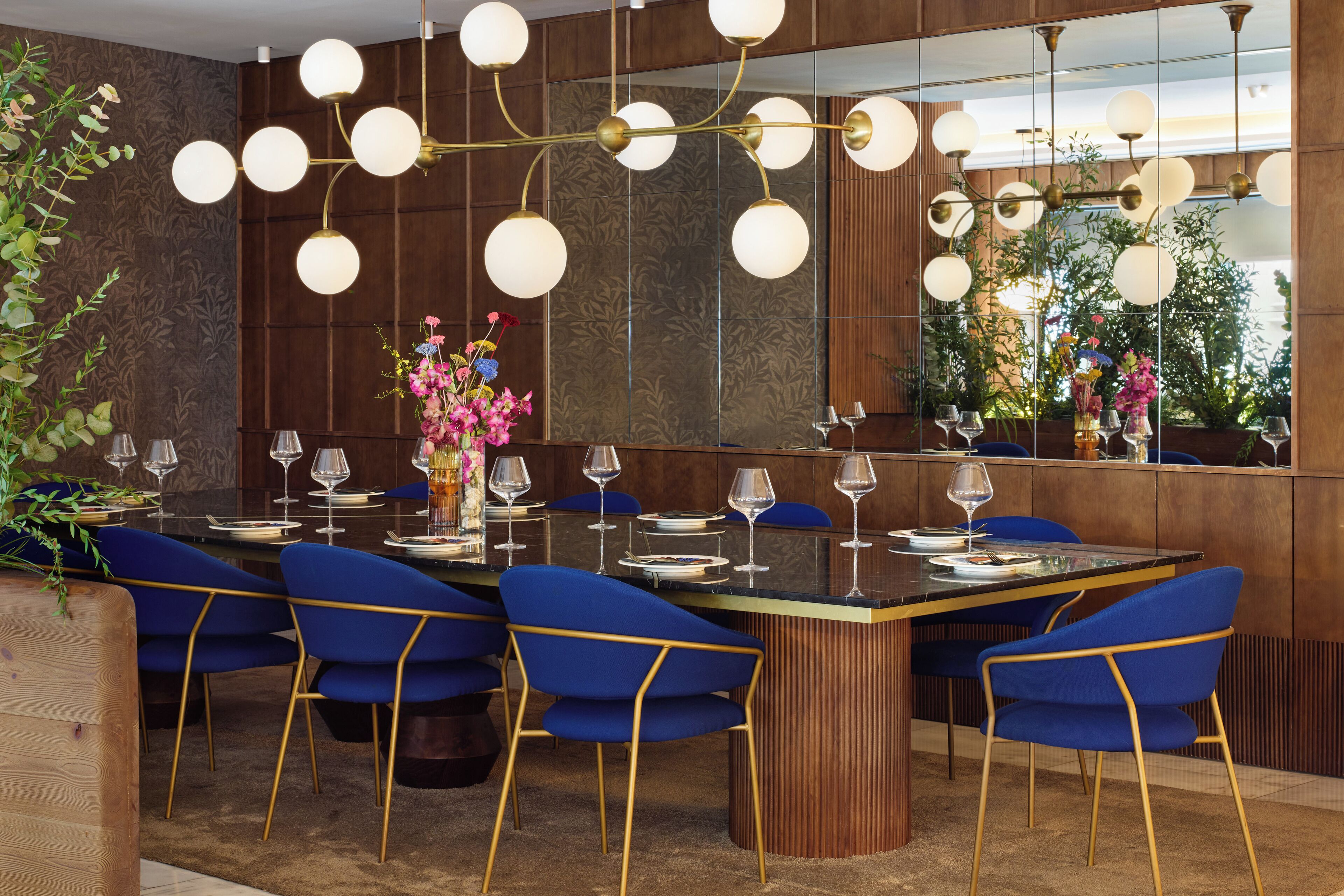 A modern dining area with a central round table, blue chairs, and a decorative light fixture.