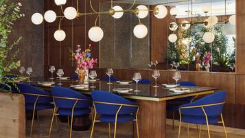 A modern dining area with a central round table, blue chairs, and a decorative light fixture.