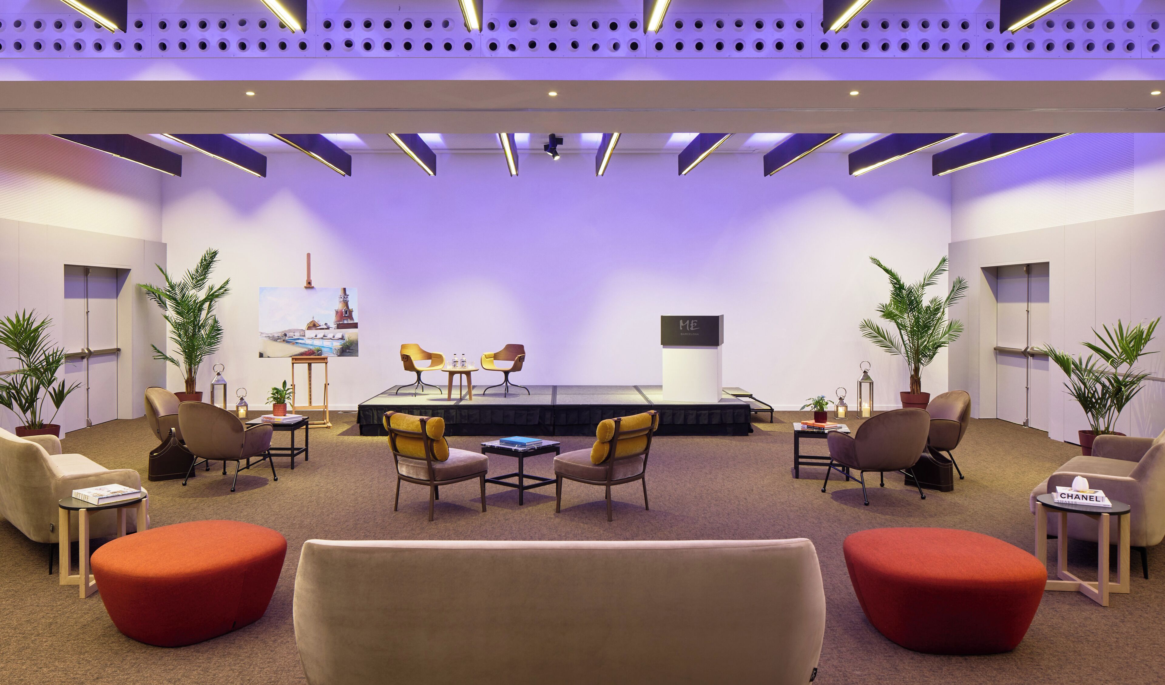Un moderno salón de conferencias con un escenario, asientos cómodos e iluminación ambiental.