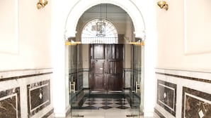 En imponerende indgang med et skakternet marmorgulv, en stor trædør og en glas elevator.