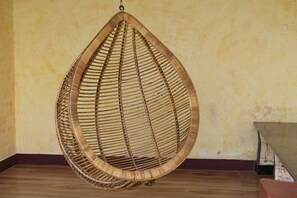 A wicker hanging chair in a room with wooden flooring and a textured wall. - Navagiraga Resorts & Hotel (Sirkazhi)