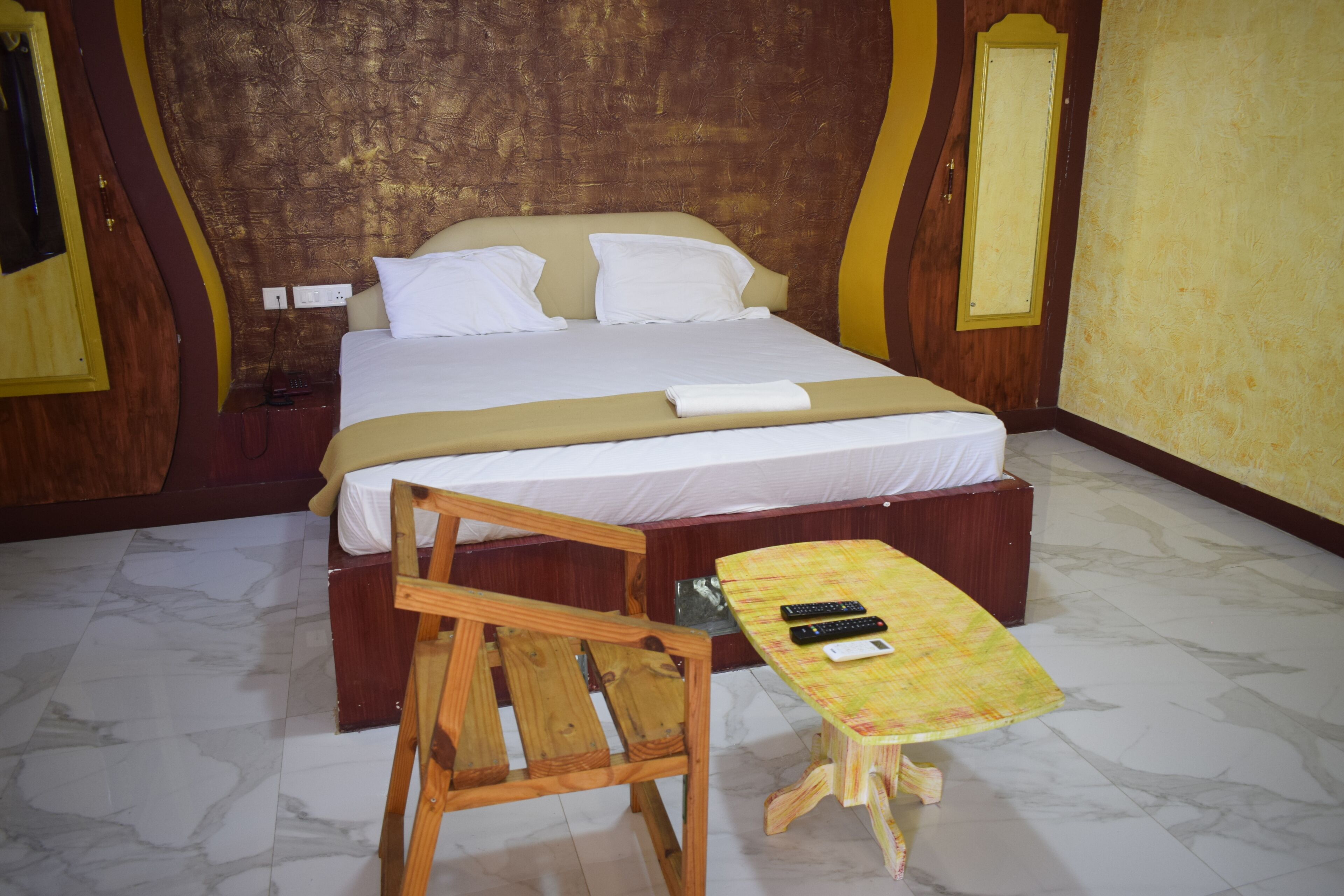 Una habitación de hotel con una cama, una silla de madera, una mesita y un control remoto sobre la mesa.