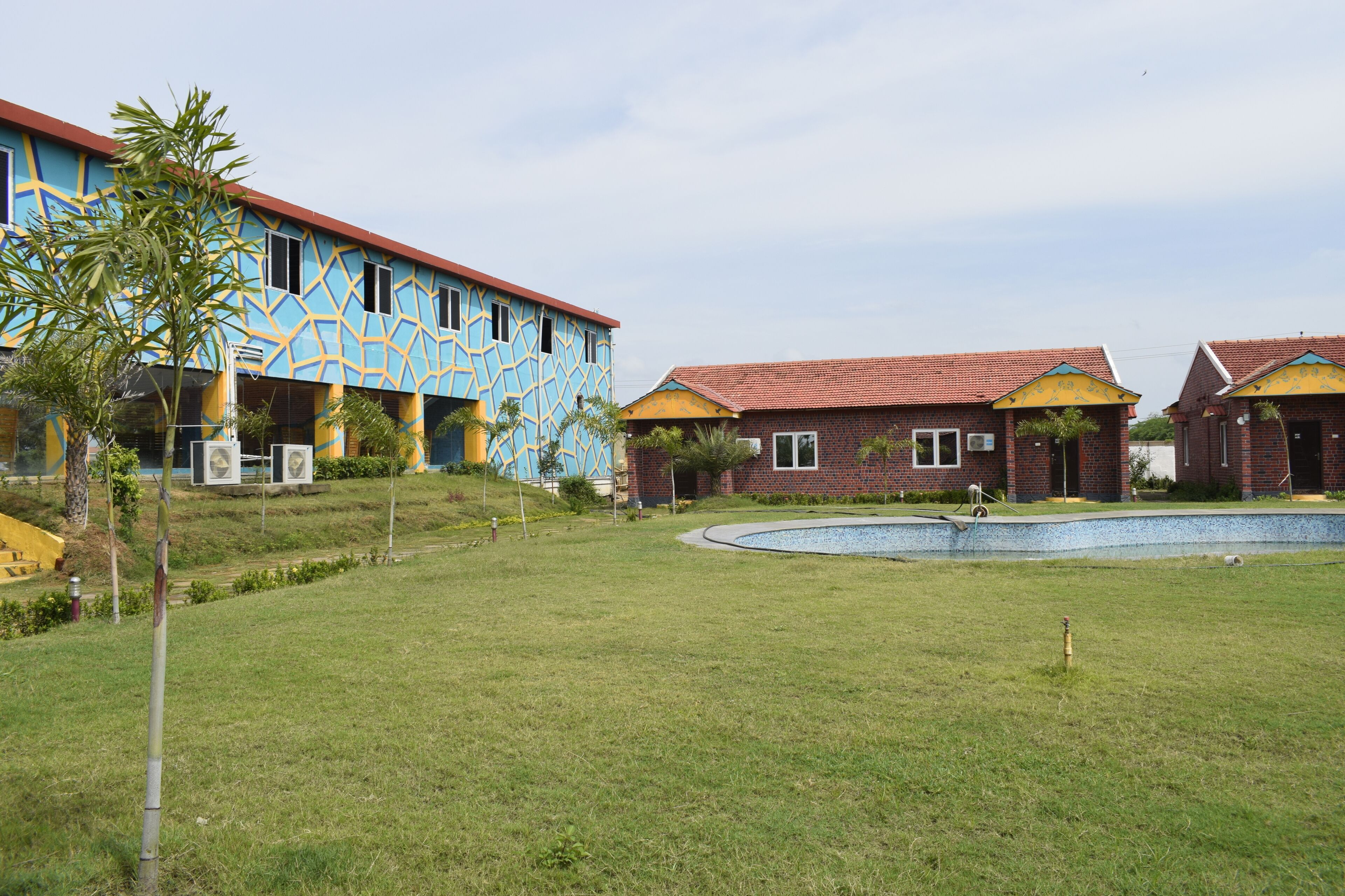 A building with a geometric pattern on its facade, a swimming pool, and a grassy area with a small tree.