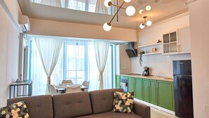 A modern living room with a sofa and a dining area, a kitchen with green cabinets and a black refrigerator, and a ceiling light fixture. - Apartament Alma Zev (Mamaia-Sat)