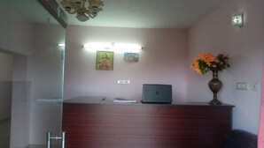 A reception desk with a laptop, a vase with flowers, and a wall-mounted light fixture. - Hotel CORNER STONE (Kodaikanal)