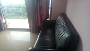 A black leather sofa in a room with a sliding glass door leading to an outdoor area. - Hotel CORNER STONE (Kodaikanal)