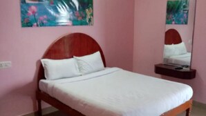 A single-bed room with a wooden headboard, a bedside table with a mirror, and a painting of a waterfall on the wall. - Hotel CORNER STONE (Kodaikanal)