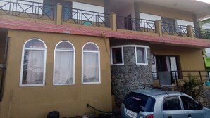 A two-story building with a stone facade, a balcony on the upper floor, and a parked car in front. - Hotel CORNER STONE (Kodaikanal)