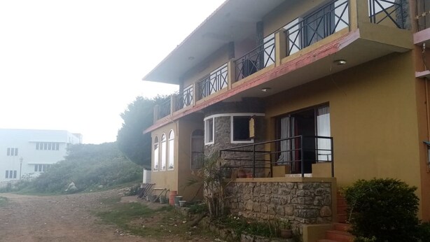 A two-story building with a stone facade, a balcony with metal railings, and a dirt road in front. - Hotel CORNER STONE (Kodaikanal)
