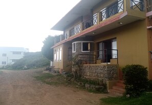 A two-story building with a stone facade, a balcony with metal railings, and a dirt road in front. - Hotel CORNER STONE (Kodaikanal)