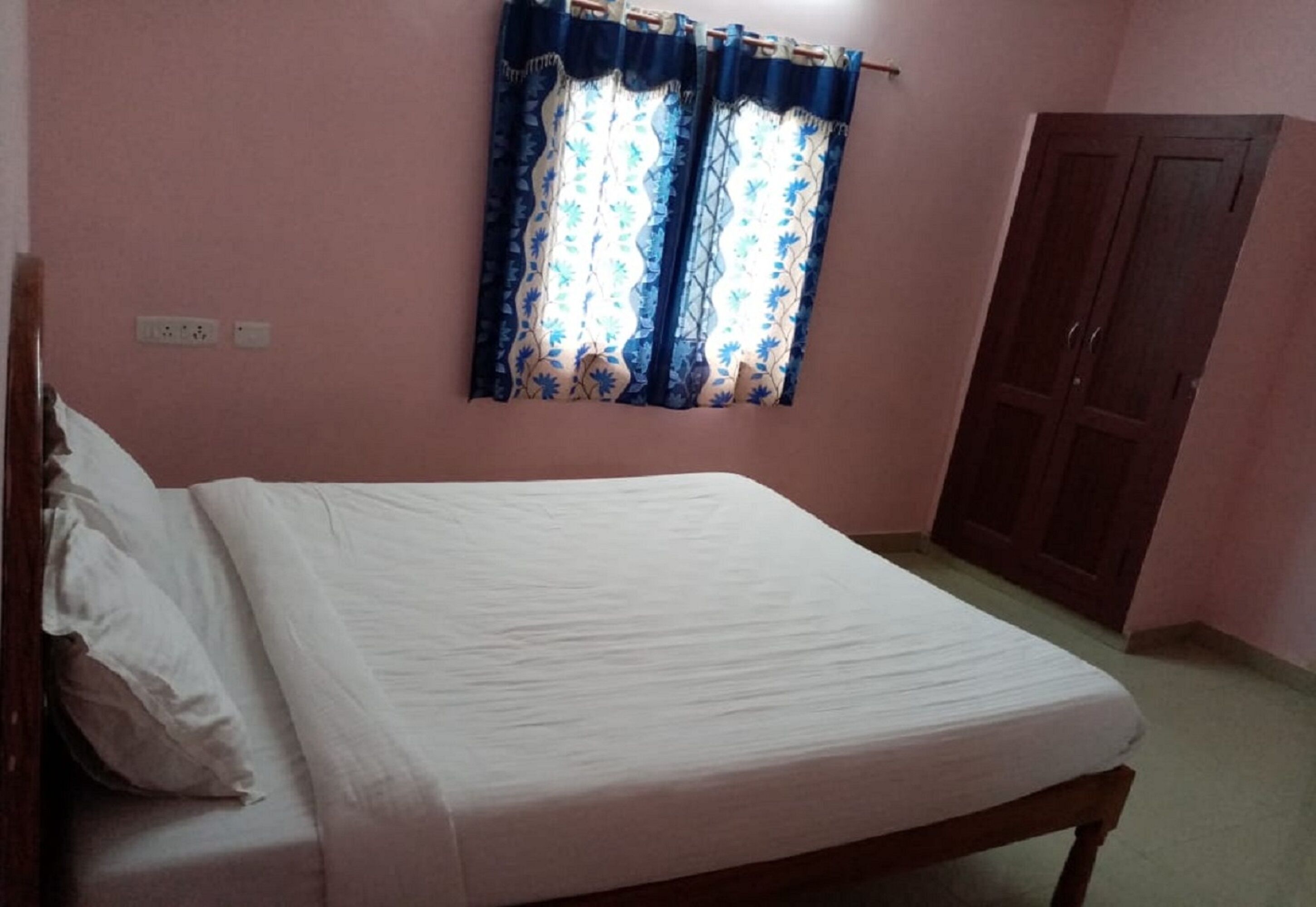 A bedroom with a bed, a wardrobe, and a window with curtains.