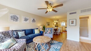 A modern living room with a blue sofa, patterned armchairs, a wooden coffee table, and a ceiling fan.