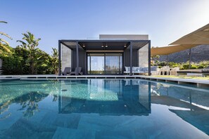 A modern outdoor pool area with clear blue water, lounge chairs, and a covered seating area. - Iniada Villa II – Beachside Retreat by etouri (Chania)