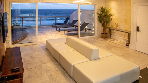 A modern living room with a white sofa, a TV, and a balcony with a view of the ocean. - Penthouse Overlooking Ipanema Beach Vsc2 (Rio de Janeiro)