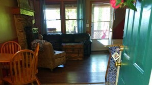 A cozy living room with a sofa, chairs, and a wooden table. A green door with a brass handle is visible, and a doormat reads "Hooray! You're here!"