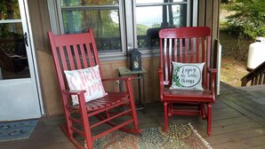Two red rocking chairs with cushions, a small table with a lantern, and a patterned rug on a wooden deck.