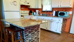 A kitchen with a granite countertop, white cabinets, a vintage microwave, and a tiled floor.