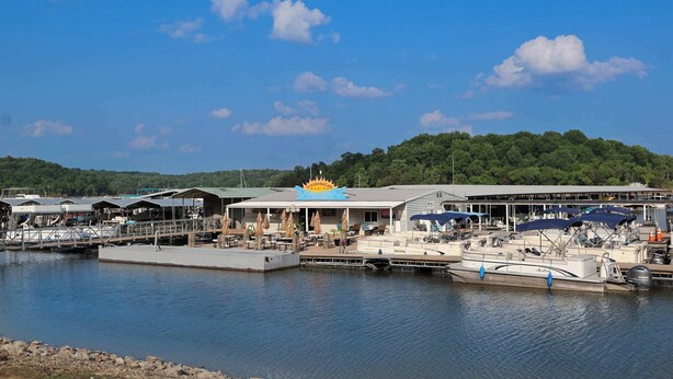Un port de plaisance avec des bateaux amarrés, un espace de repos abrité et un bâtiment orné d’un emblème solaire distinctif.