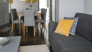 A living room with a grey sofa, a dining table with chairs, a chandelier, and a framed picture on the wall. - Deluxe 4 bedroom house (Harrogate)