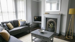 A living room with a grey sofa, a coffee table, a fireplace, and a TV. - Deluxe 4 bedroom house (Harrogate)