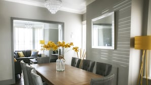 A dining area with a wooden table, grey upholstered chairs, and a vase with yellow flowers. - Deluxe 4 bedroom house (Harrogate)