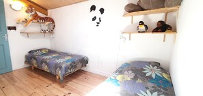 Ein Schlafzimmer mit zwei Betten, Holzboden, einer Wanddekoration mit einem Tiger und Regalen mit Stofftieren.