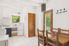 Een kleine keuken met witte kastjes, een houten eettafel en een hanglamp.