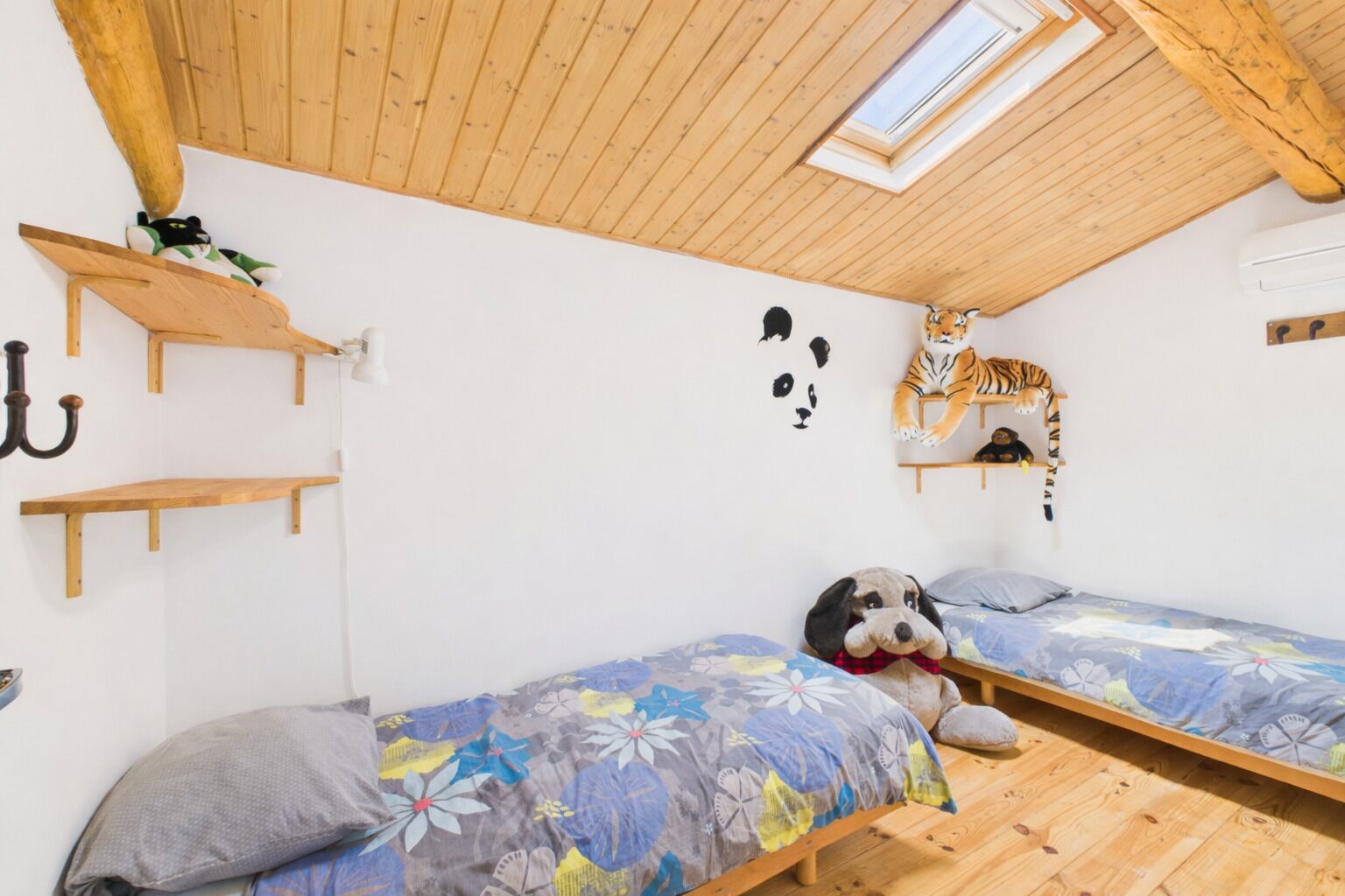 A small, cozy room with two beds, wooden beams on the ceiling, and a skylight.