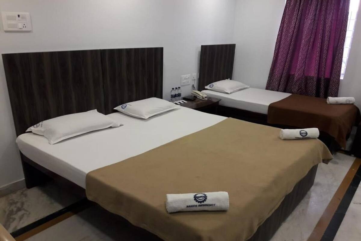 A hotel room with two beds, each with a pillow and a blanket. There is a small table with a phone and a bottle of water.