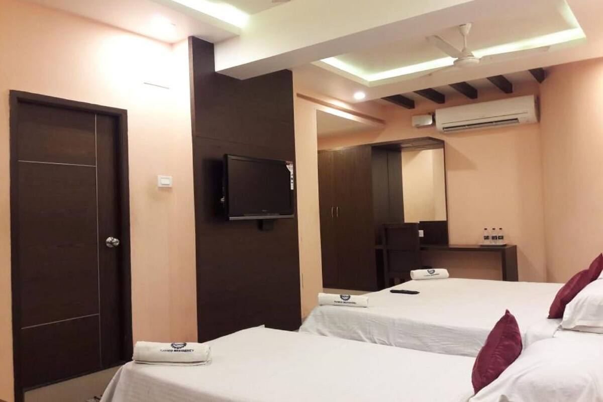 A hotel room with two single beds, a television mounted on the wall, a mirror above the bed, and an air conditioning unit on the wall.