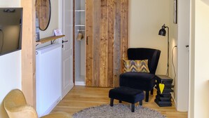 Un salon chaleureux avec un plancher en bois, un canapé noir, un fauteuil jaune et un tapis gris.