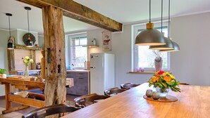 Une cuisine moderne avec des poutres en bois, une longue table à manger et des luminaires suspendus.