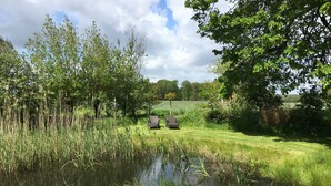 Un étang bordé d’une végétation luxuriante et d’arbres, avec deux chaises placées face à l’eau.