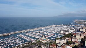 A marina with numerous boats docked, surrounded by buildings and a clear view of the sea.
